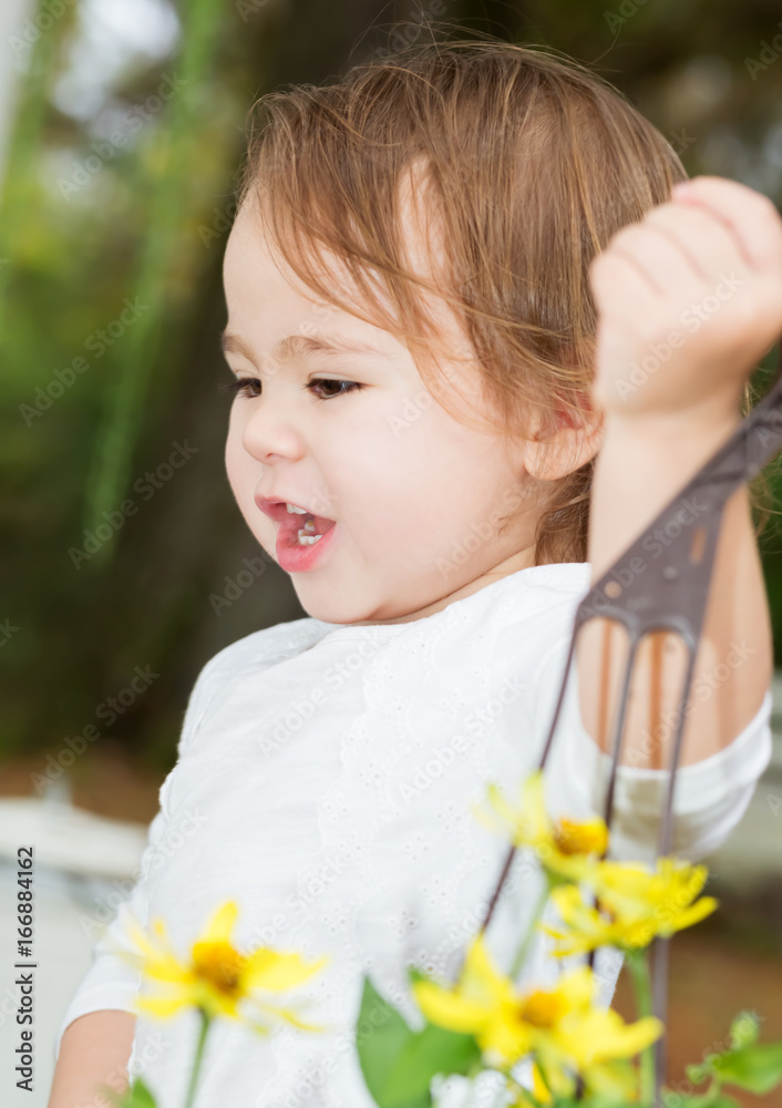 Happy toddler girl happily playing outside with flowers