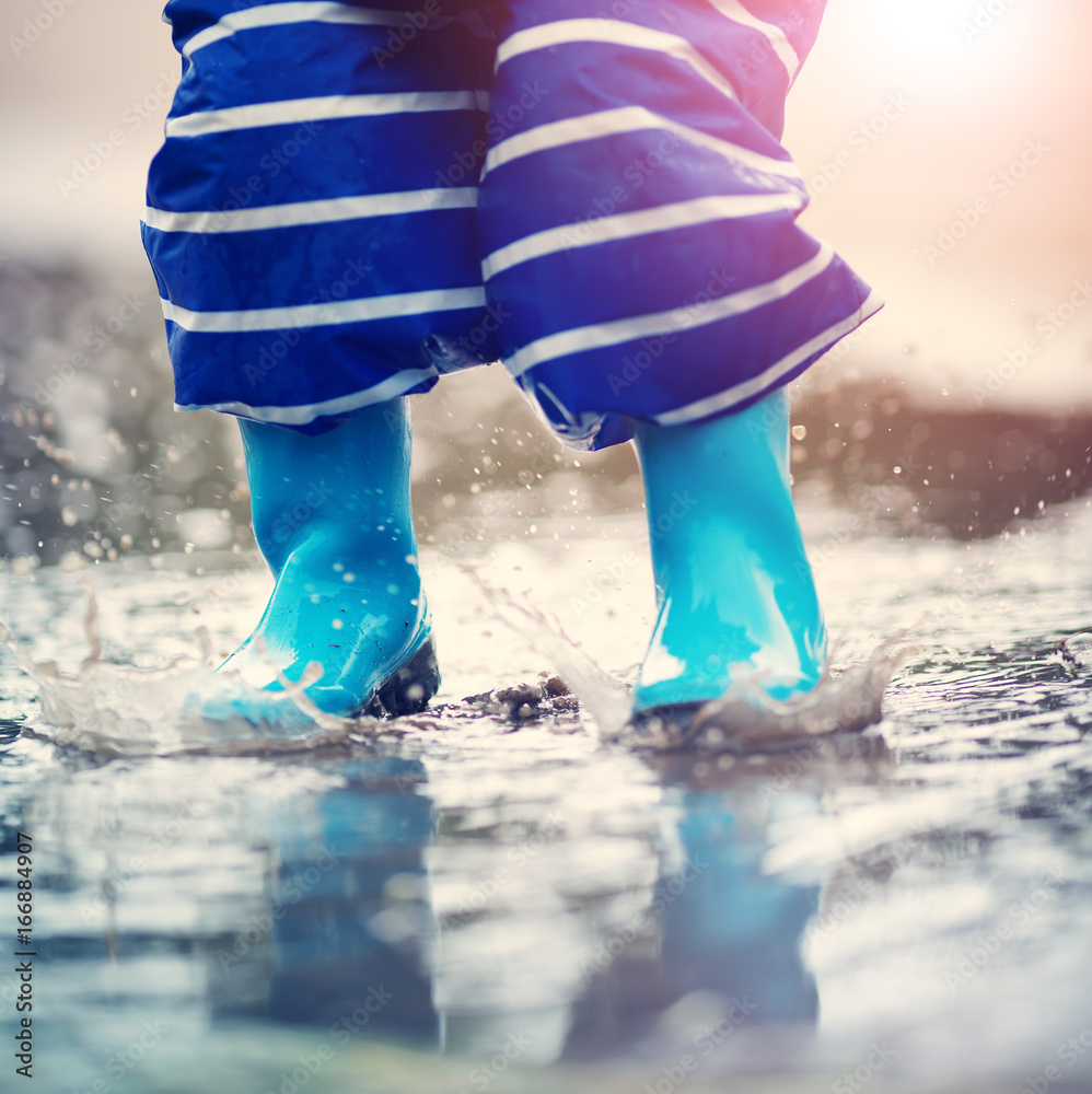 雨天孩子穿着雨鞋在水坑里行走