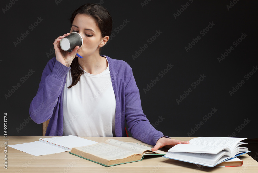 attractive brunette female student on class desk drinking coffee and reading education book