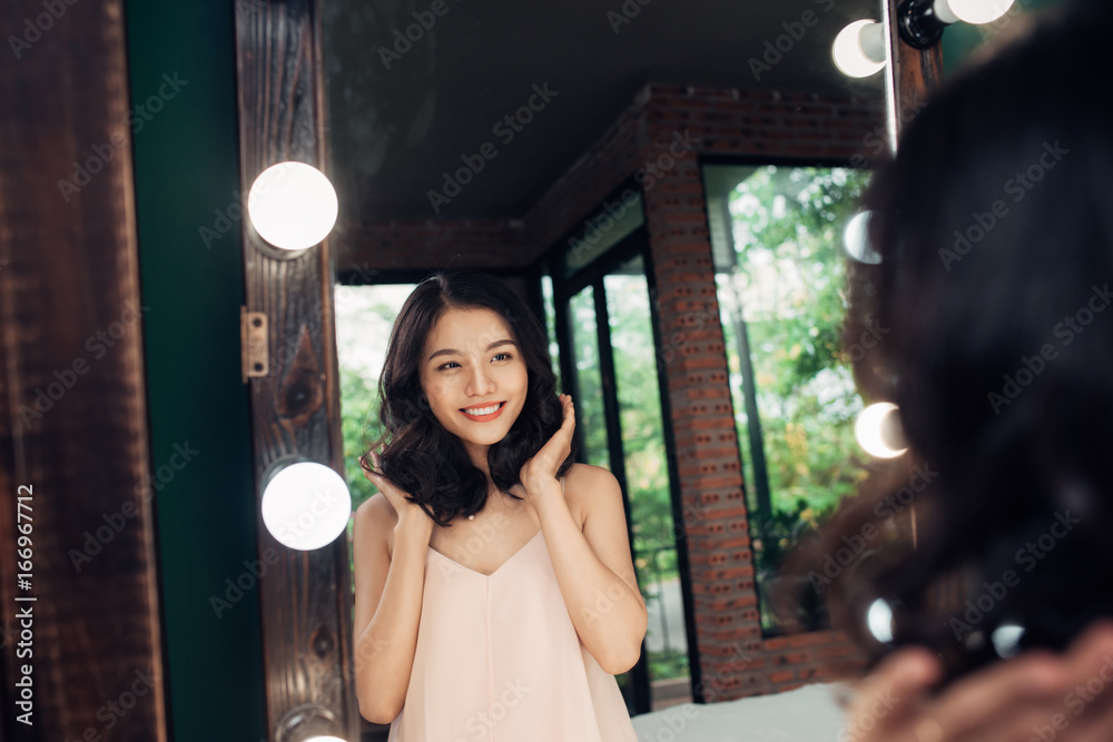 Young woman looking herself reflection in mirror at home.