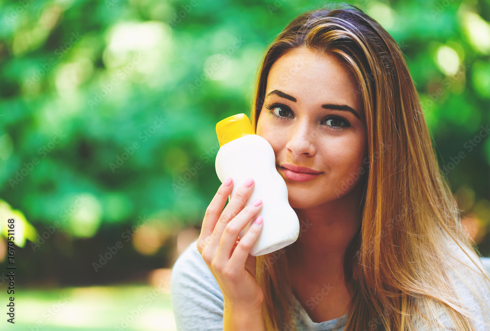 Young woman a bottle of sunblock outside on a summer day