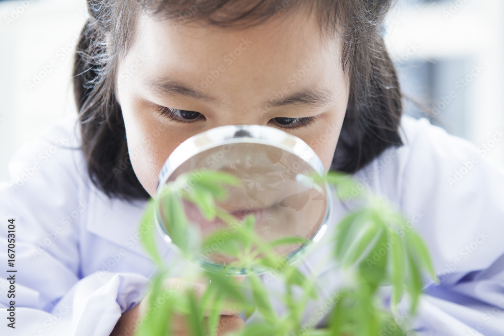 A girl in a white suit watches a plant with a magnifying glass