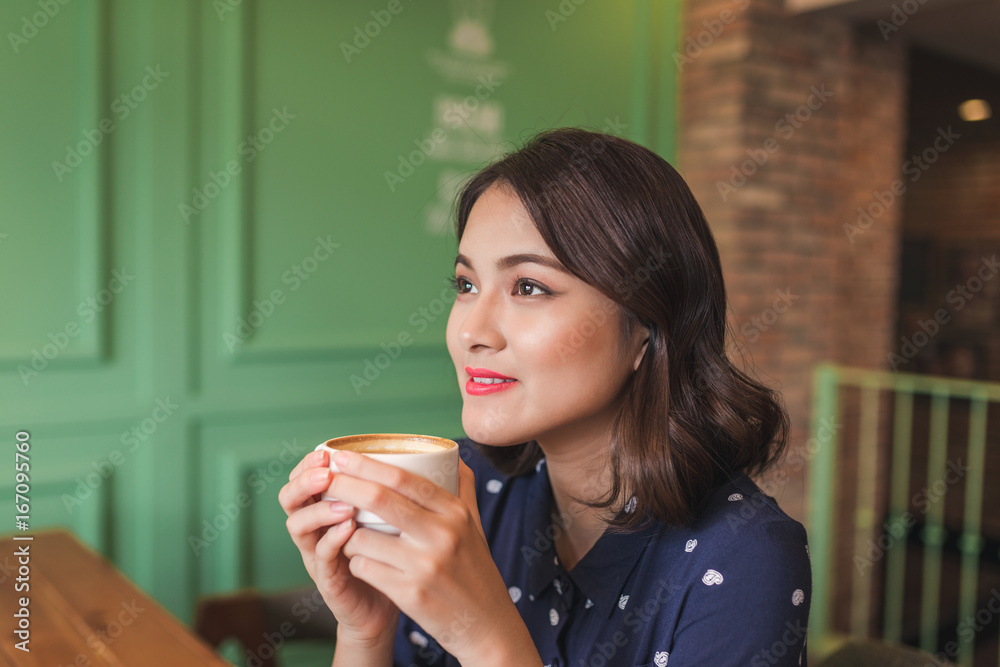 Portrait of happy young business woman with mug in hands drinking coffee in the morning at restauran