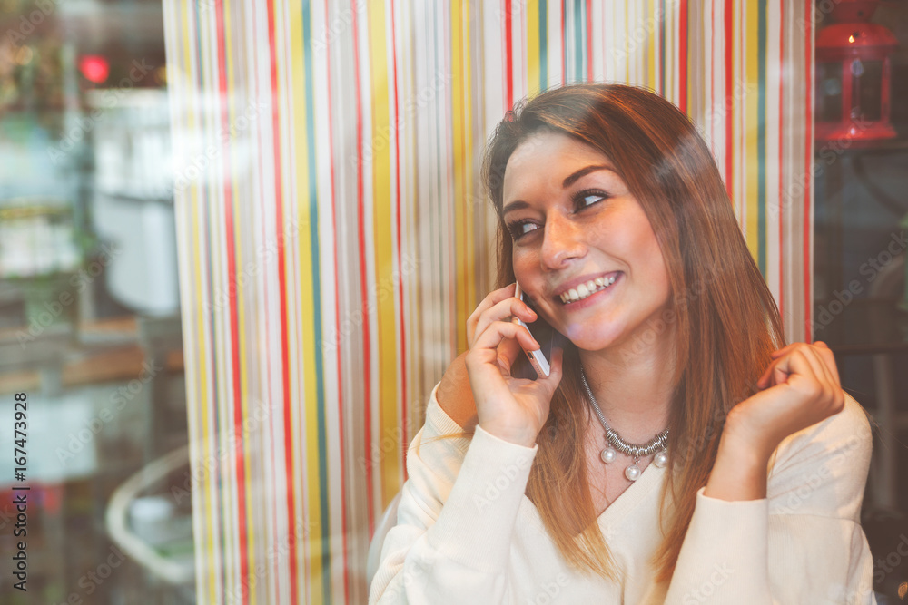 Girl talking on mobile phone in cafe at shopping mall