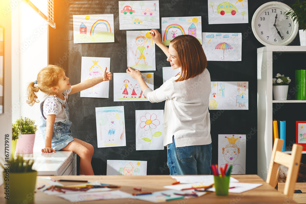 Mother and child girl hang their drawings on wall