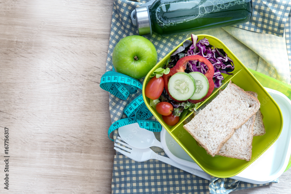 The Healthy Lunch box with grain bread and green vegetable and fruit juice bottle on wooden backgrou