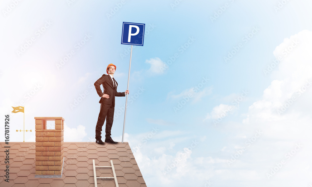 Young businessman with parking sign standing on brick roof. Mixed media