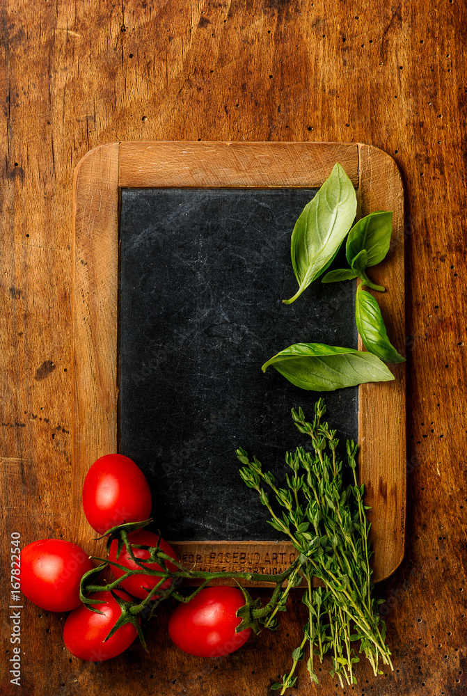 Thyme and basil leaves with tomatoes on chalkboard. Wooden background. Copy space for design. Top vi