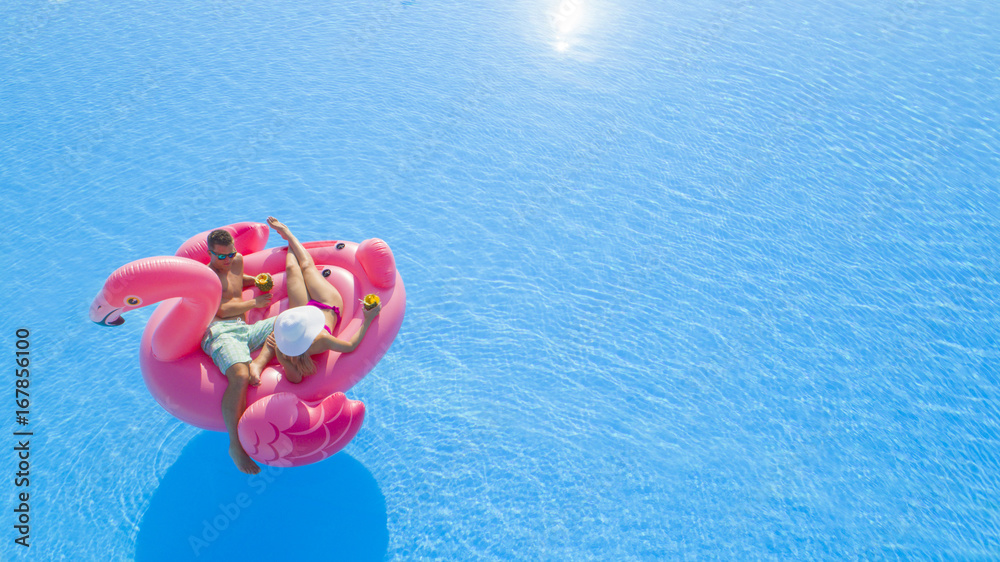 AERIAL CLOSE UP Beautiful young couple drinking cocktails, relaxing, lying on fun inflatable pink fl