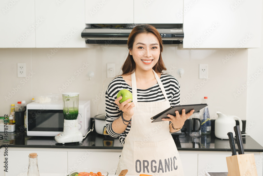 年轻的亚洲女人在厨房里用平板电脑做饭