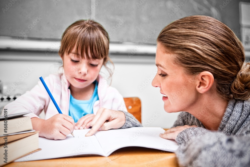 Schoolgirl writing with her teacher in classroom