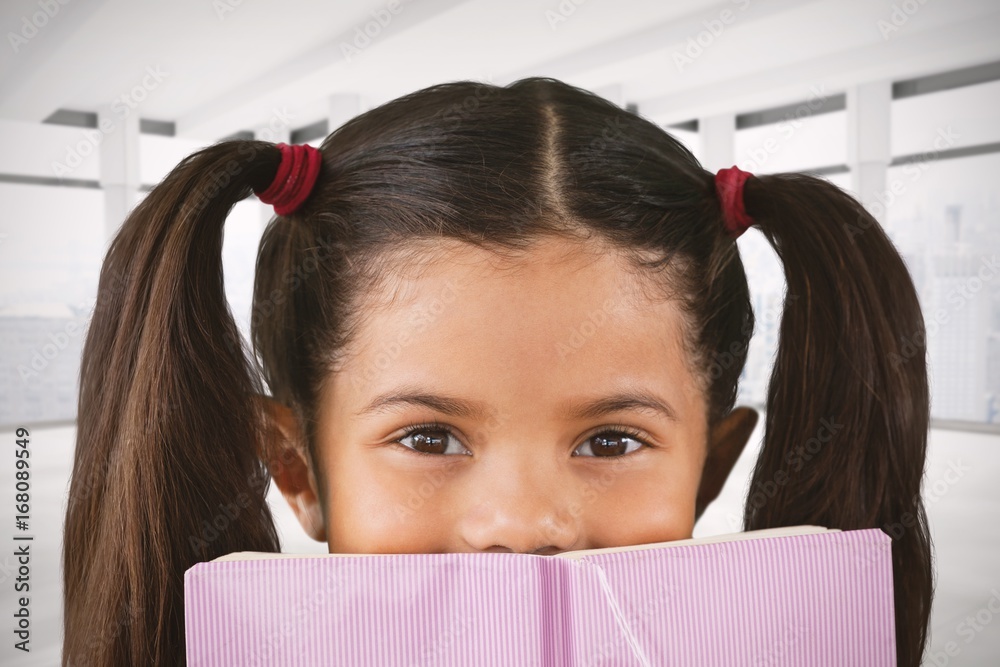 Composite image of schoolgirl covering mouth with book