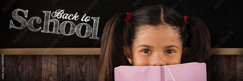 Composite image of schoolgirl covering mouth with book