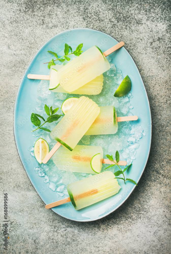 Summer refreshing lemonade popsicles with lime and mint with chipped ice on blue plate over grey con