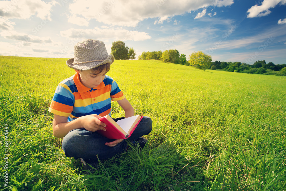 eight years old child reading a book sitting on the grass