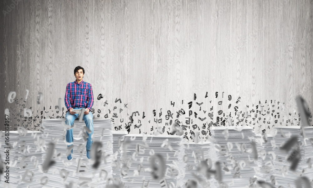 Attractive man sitting on pile of paper documents.