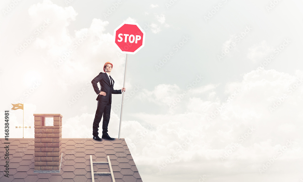 Caucasian businessman on brick house roof showing stop road sign