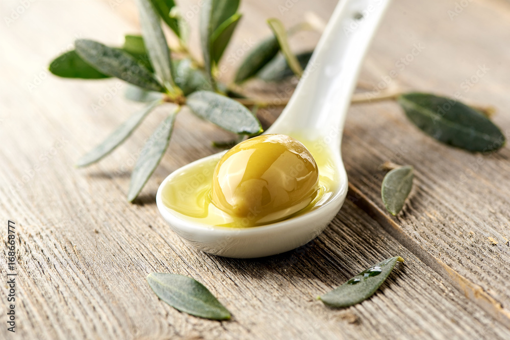 Olives, olive oil and olive branch on wooden light table.