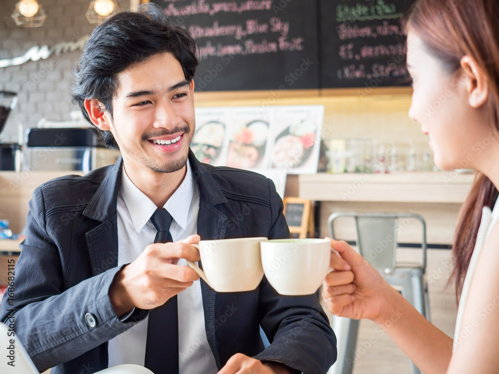 Two of young businessman / woman in casual suit talking and drinking coffee during meeting at cafe