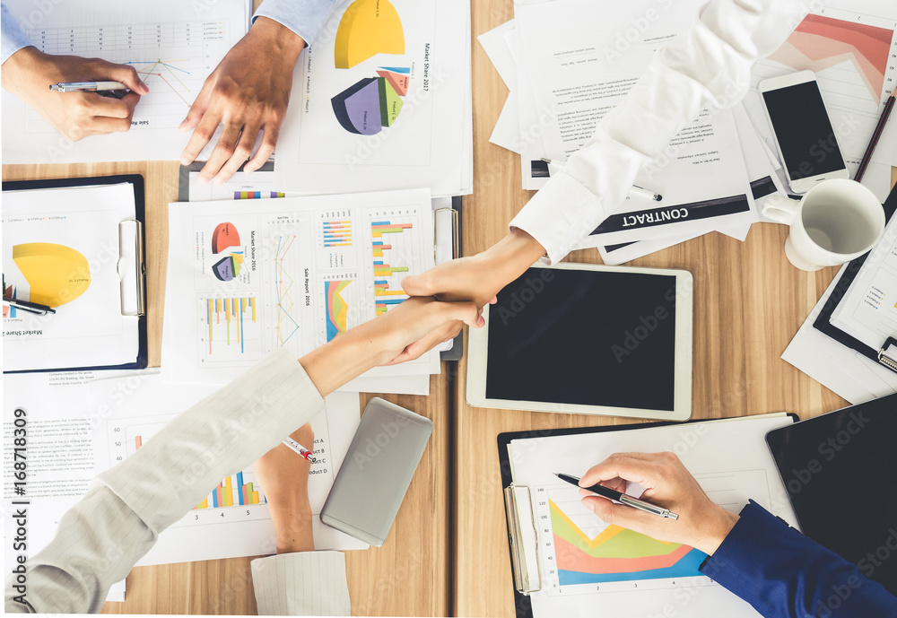 Businesswoman shaking hands during meeting on meeting table/desk with many financial documents, team