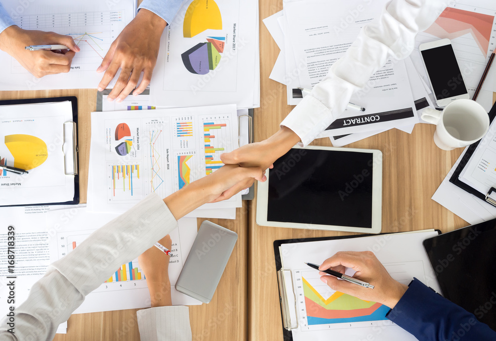 Businesswoman shaking hands during meeting on meeting table/desk with many financial documents, team