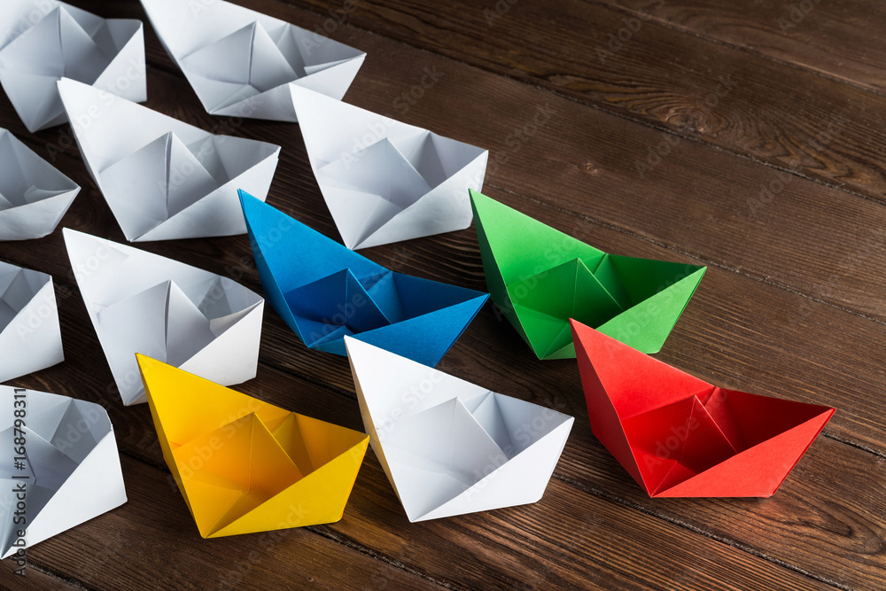 Business leadership concept with white and color paper boats on wooden table