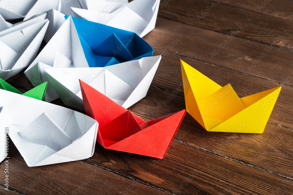 Business leadership concept with white and color paper boats on wooden table