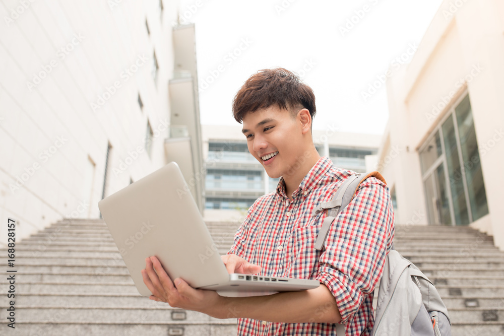 年轻人拿着笔记本电脑坐在大学大楼外