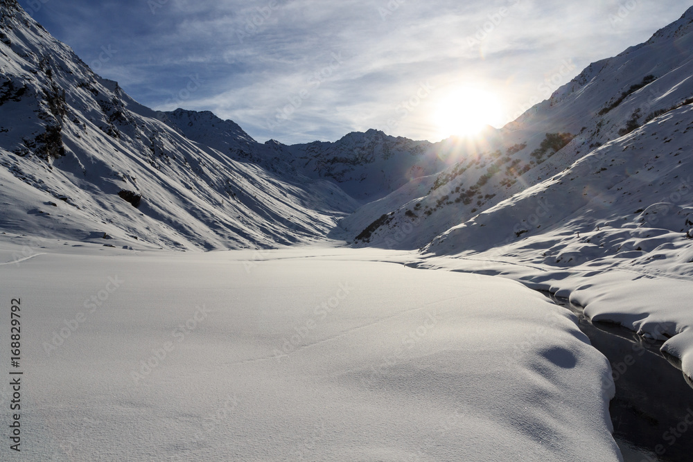 Mountain panorama with snow, small river and sun in winter in Stubai Alps, Austria