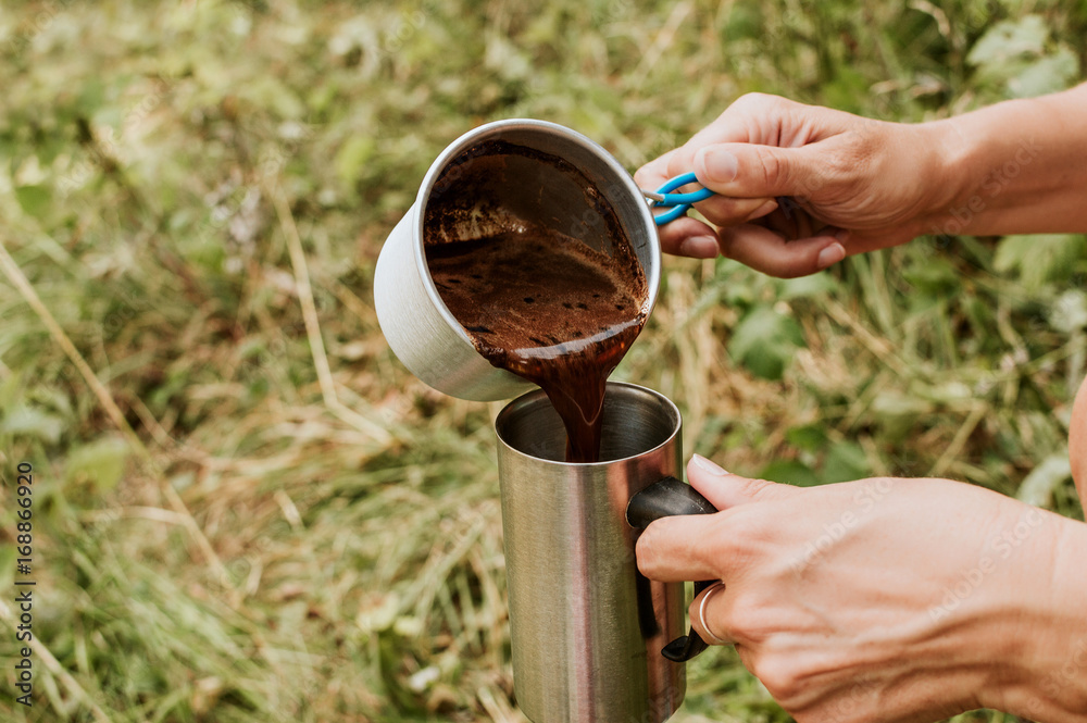 Woman in a pours hot coffee in the cup, outdoors.