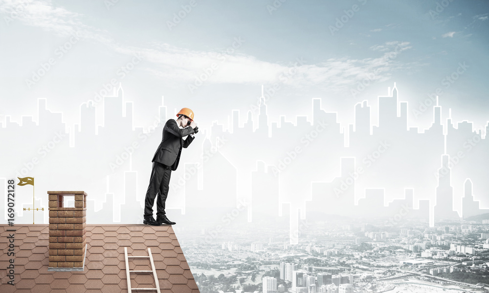 Engineer man standing on roof and looking in binoculars. Mixed m