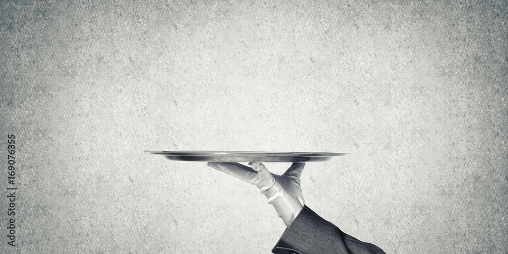 Hand of butler holding empty metal tray against concrete background