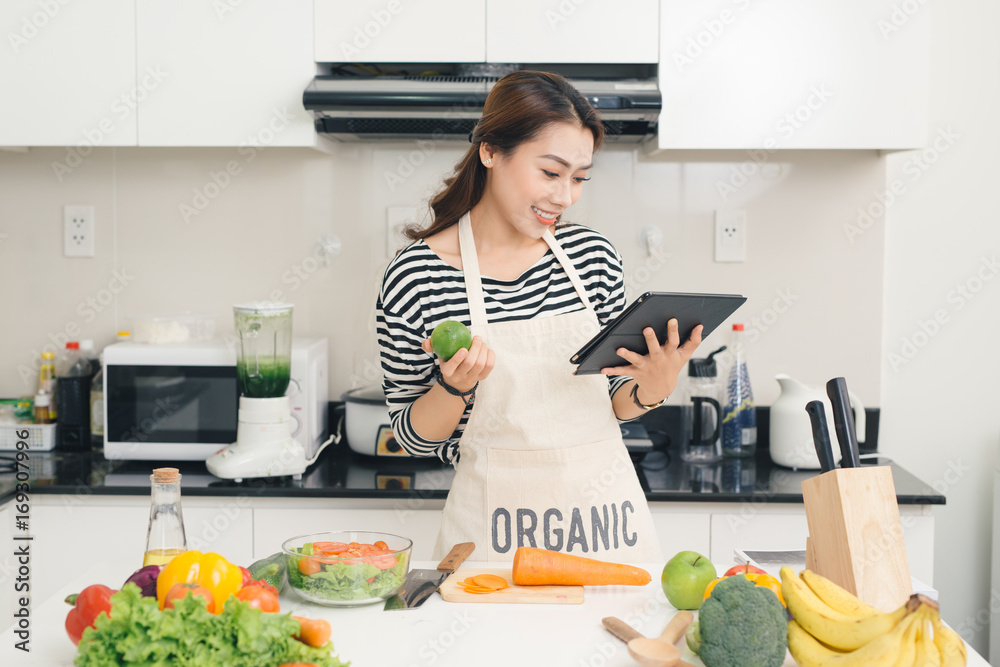 年轻的亚洲女人在厨房里用平板电脑做饭