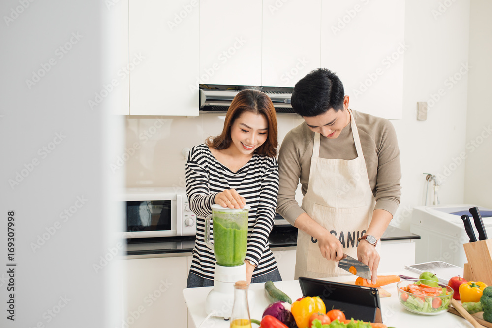 幸福的亚洲年轻夫妇在家里的厨房里一起做饭的画像。