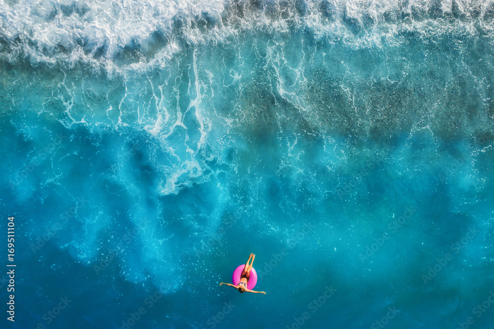 Aerial view of young woman swimming on the pink swim ring in the transparent turquoise sea in Oluden