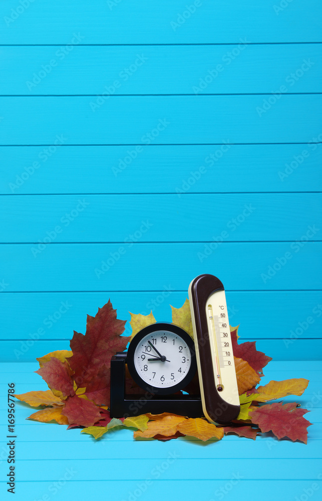 Autumn leafs and alarm clock on wood