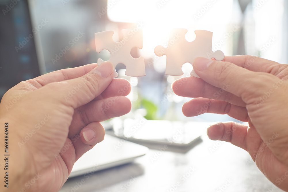 Young businessman trying to connect couple puzzle piece with sun flare and blur background,symbol of