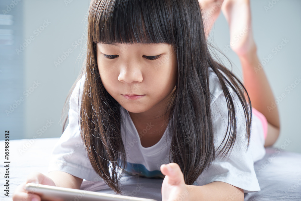 Little asian chinese girl using smartphone and lying on the bed .