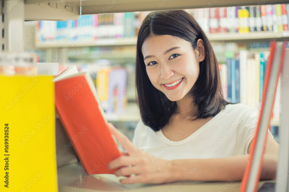 快乐的亚洲女学生在课间休息时在现代的书架旁看书