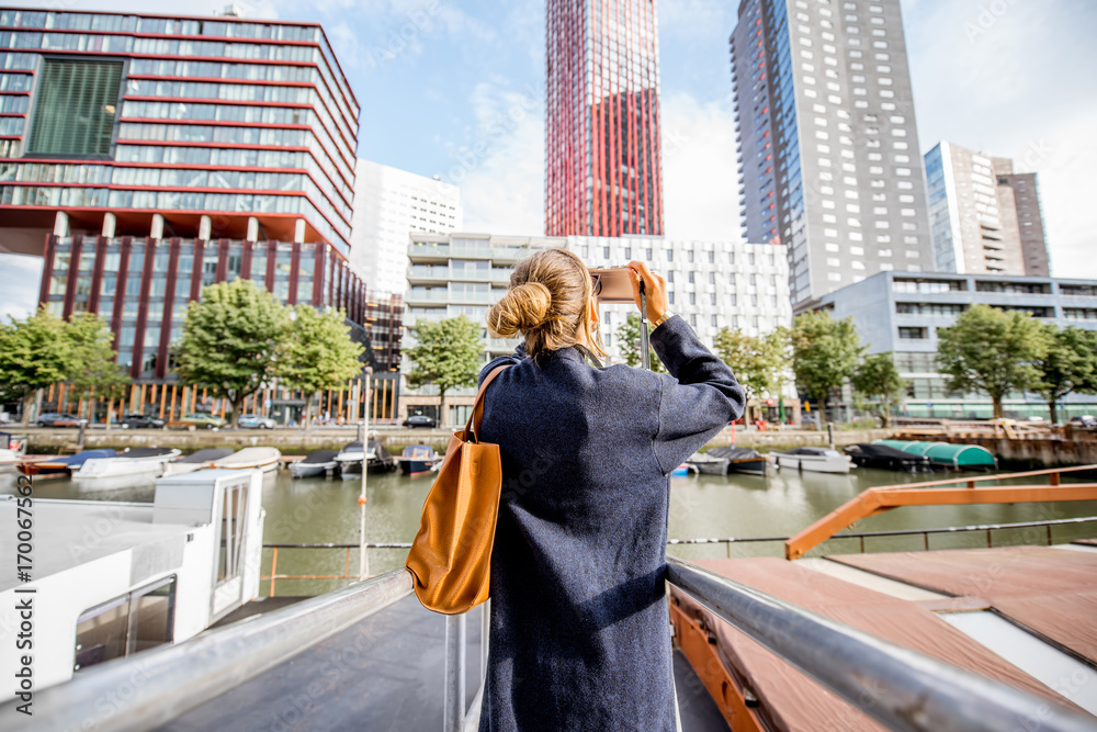 Young woman photographing modern skyscrapers standing on the harbor in Rotterdam city