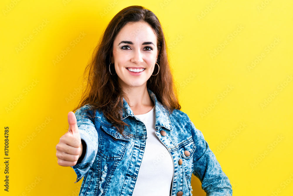 Happy young woman giving a thumb up on a yellow background