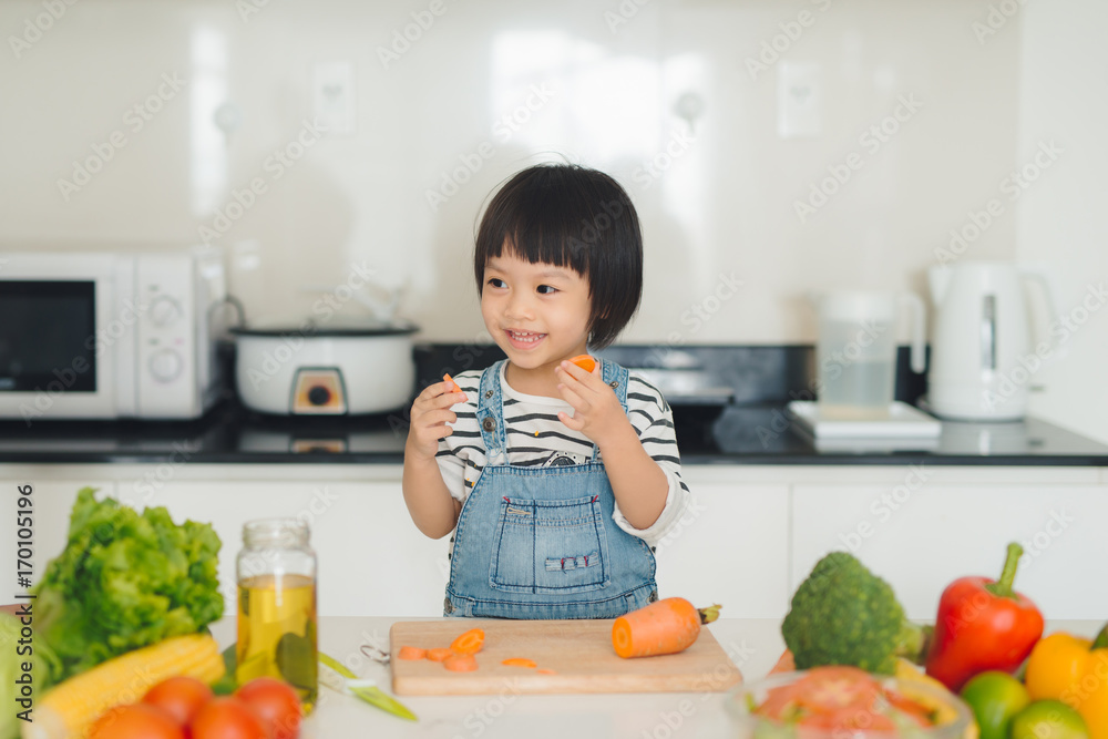 小女孩用胡萝卜玩得很开心。家庭厨房内部有水果和蔬菜。