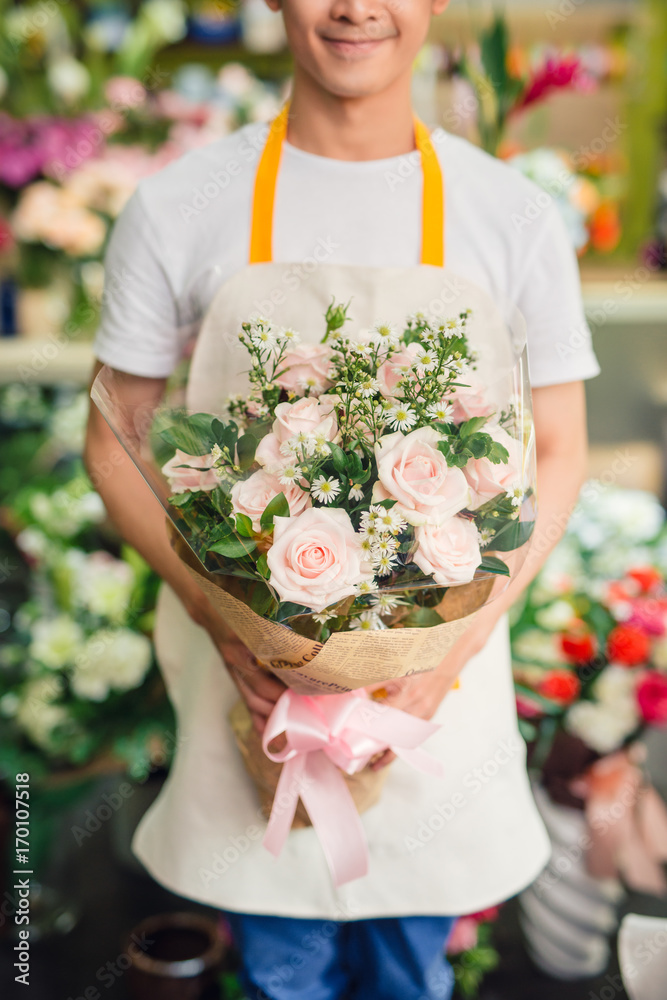 英俊的男花商站在花店里，手里拿着一束花