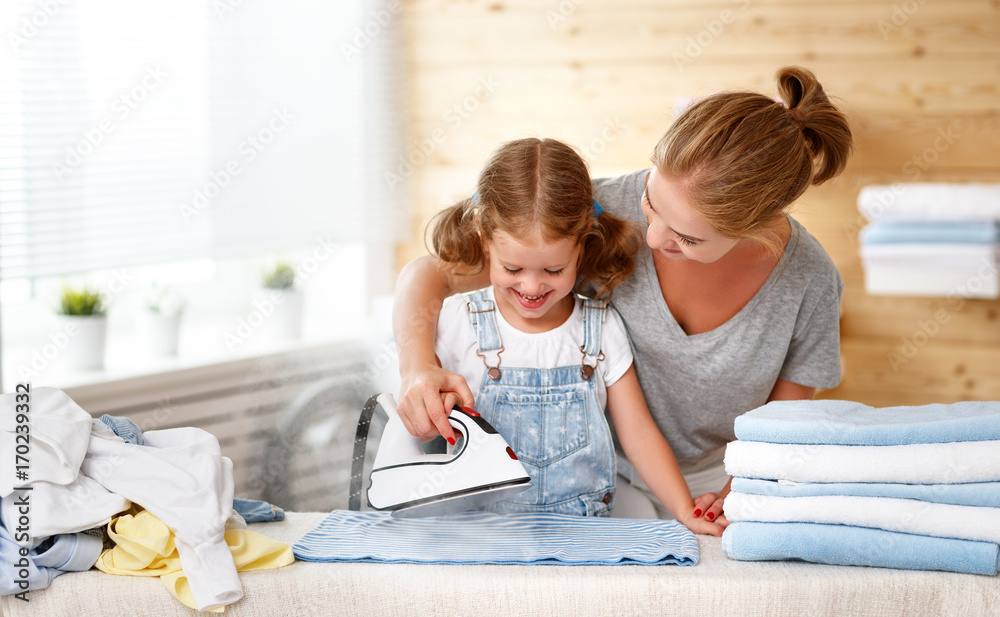 Happy family mother housewife and child daughter ironing clothes   in laundry