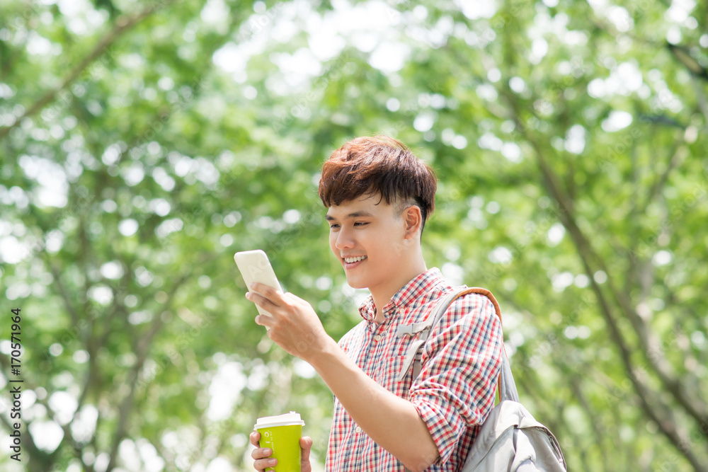 年轻的亚洲男子在公园里微笑着打电话