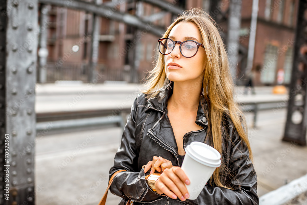 Lifestyle portrait of a stylish business woman checking time standing outdoors with coffee cup on th