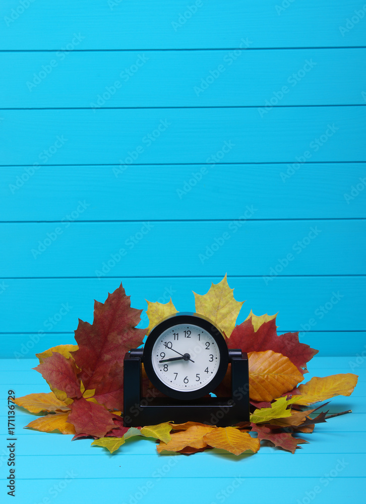 Autumn leafs and alarm clock on wood