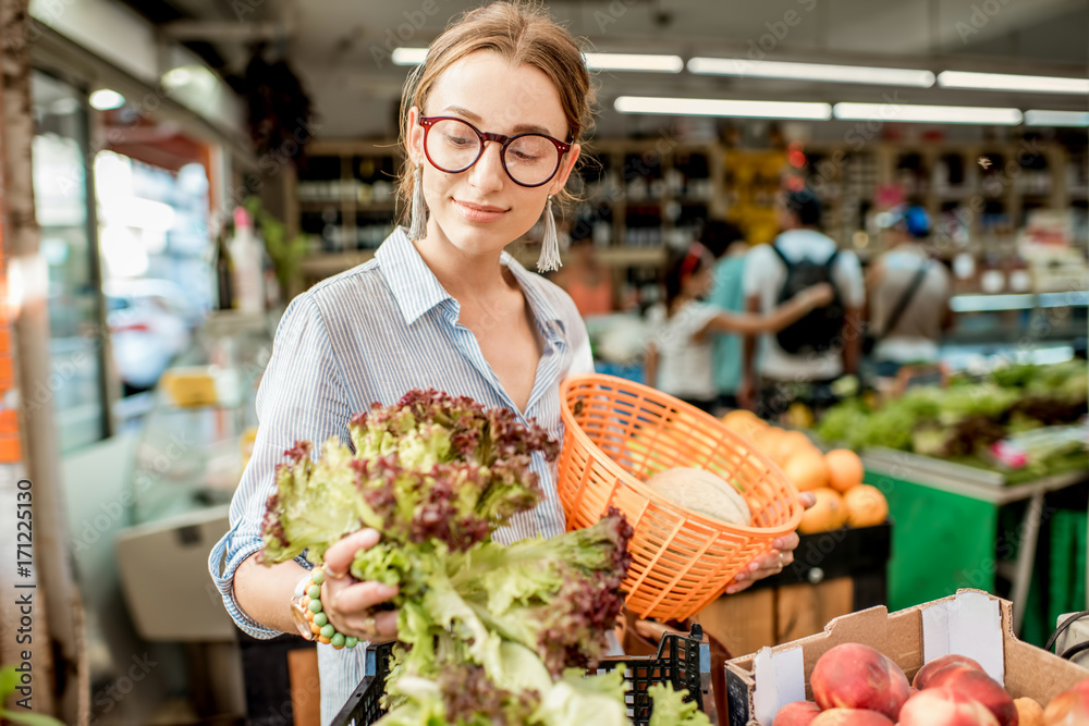 Young woman choosing a fresh salad standing with basket at the food market in France