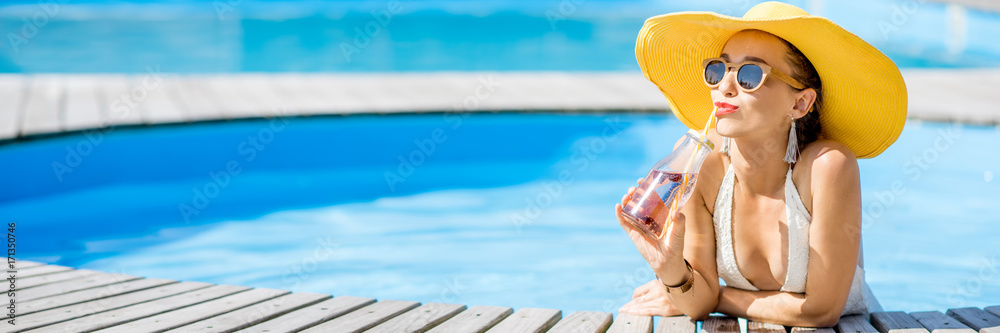 Young woman in swimsuit with big yellow sunhat relaxing with a bottle of fresh drink sitting on the 