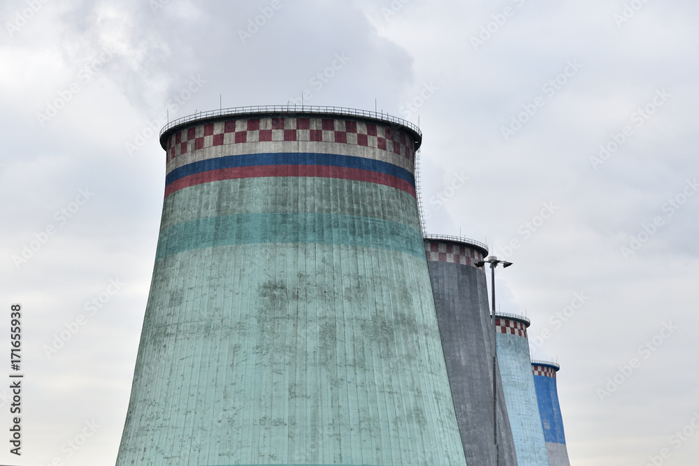 Large pipes of the heat station smoke against the sky with clouds